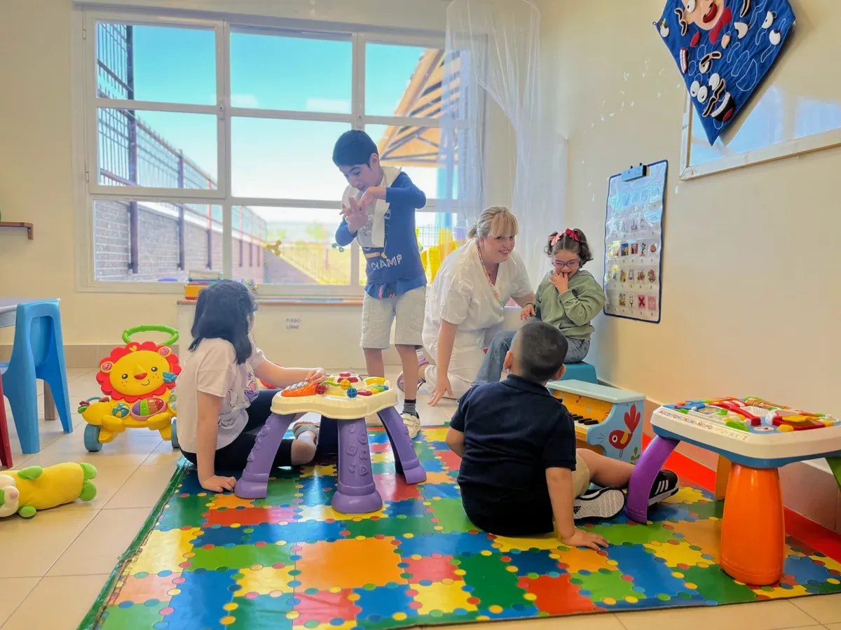 Una profesional juega con varios alumnos sobre una alfombra de colores en un aula del Colegio de Educación Especial San José