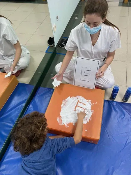 Niño trazando una letra en espuma durante una actividad sensorial con su terapeuta
